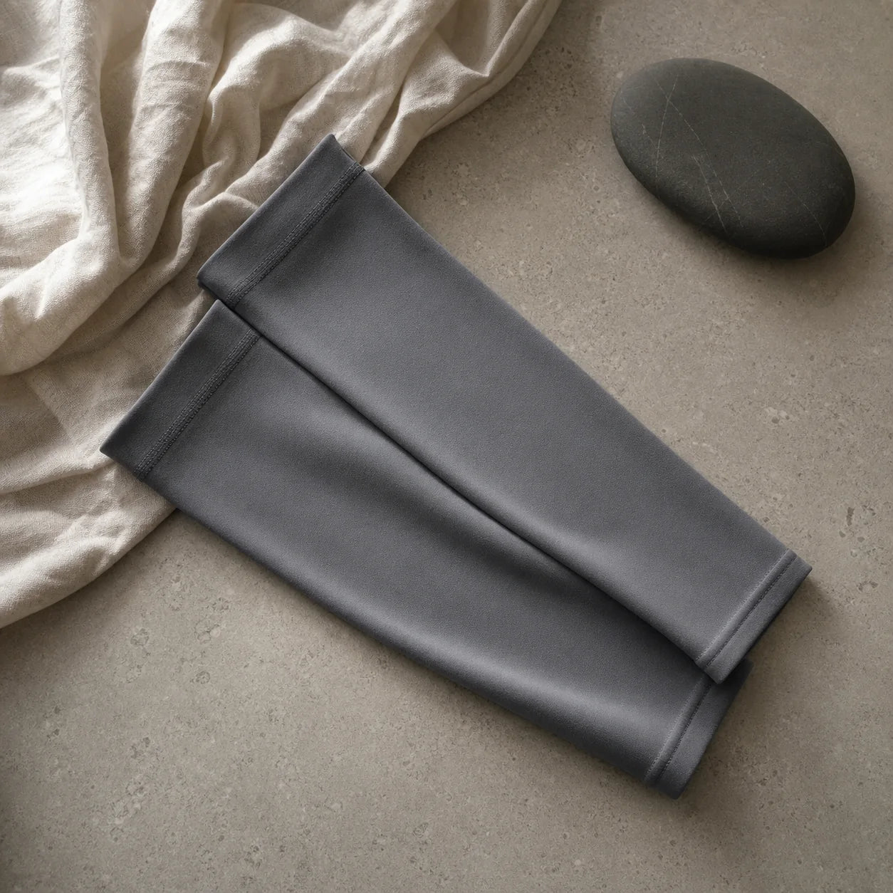 Folded slate-grey arm sleeves on a warm stone surface